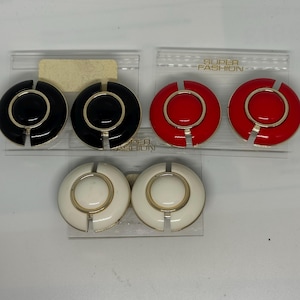 Op de afbeelding: Drie paar vintage clip-on oorbellen in zwart, rood en wit. Elke oorbel heeft een cirkelvormig ontwerp met een goudkleurig midden en accenten. De verpakking leest "SUPER FASHION".