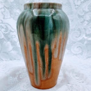 May include: A ceramic vase with a rounded body and a narrow neck. The vase features a color gradient, with green and brown tones dripping over an orange base. The glaze gives a glossy finish to the handmade pottery.