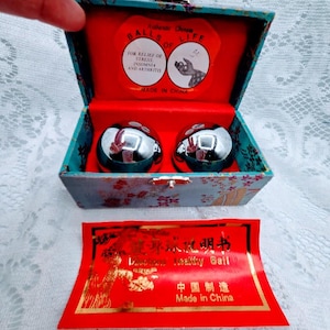 May include: A teal and red box with two shiny silver balls inside. The box has text that reads "BALLS OF LIFE" and "FOR RELIEF OF STRESS, INSOMNIA AND ARTHRITIS." A red card with Chinese text and "Healthy Ball" is also present.