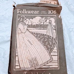 Pode incluir: Um envelope de padrão Folkwear vintage, número 106, para um casaco turco. A capa apresenta uma ilustração em tons sépia de uma mulher com o casaco. O envelope é castanho com as palavras "Turkish Coat" e "Pattern Sewing Instructions Quilting Design".