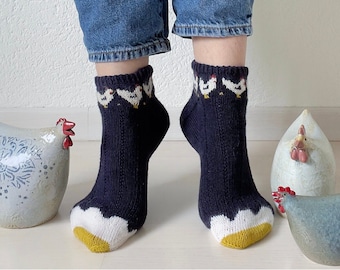 Puede incluir: Un par de calcetines azul oscuro con un patrón de pollo blanco. Los calcetines están doblados hacia abajo para mostrar el patrón. Los calcetines están en los pies de una persona.
