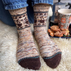 Puede incluir: Un par de calcetines de punto marrón y beige con un puño estampado en marrón y azul. Los calcetines están sobre una superficie blanca y esponjosa.