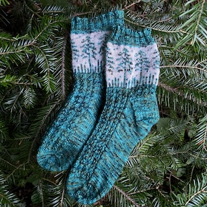May include: A pair of teal and green knitted socks with a white and green tree pattern on the top of the socks.