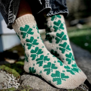 Può includere: Un paio di calze di lana con un motivo a trifoglio verde su sfondo beige. Le calze sono indossate ai piedi.