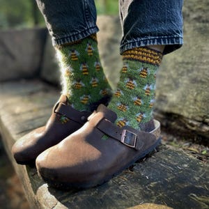 May include: A pair of brown leather clogs with green and yellow socks featuring a bee pattern. The socks are made of a soft, fuzzy material.