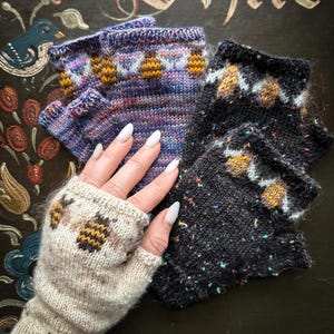 Könnte beinhalten: Drei Paar Fingerlose Handschuhe mit einem Bienenmuster. Ein Paar ist schwarz mit weißen und gelben Akzenten, ein Paar ist lila mit weißen und gelben Akzenten und ein Paar ist beige mit braunen und gelben Akzenten.