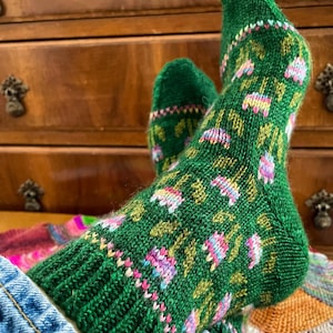 Puede incluir: Un par de calcetines de punto verde con un patrón floral en rosa, azul y blanco. Los calcetines se llevan puestos en los pies.