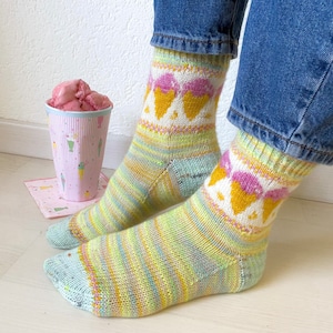 May include: A pair of colorful knitted socks with an ice cream cone pattern. The socks are light blue, yellow, and pink with white accents. The socks are worn on a person's feet.