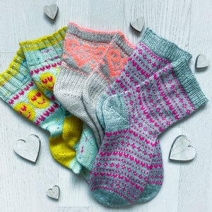 Puede incluir: Cuatro pares de calcetines de punto coloridos con diferentes patrones. Los calcetines están hechos de hilo suave y tienen una variedad de colores, incluyendo rosa, azul, amarillo y gris.