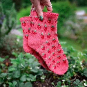 May include: A pair of pink socks with a strawberry pattern. The socks are made of a soft, knitted fabric and are perfect for everyday wear.
