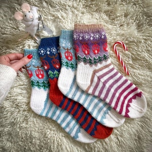 Peut inclure: Quatre paires de chaussettes tricotées colorées sur le thème des fêtes d'hiver. Les chaussettes présentent un fond blanc avec des rayures rouges, bleues et violettes et un motif de sapins de Noël et de décorations.