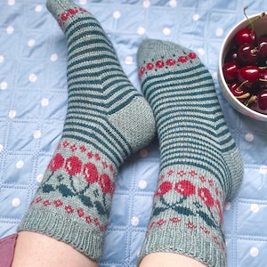 Peut inclure: Une paire de chaussettes rayées bleu sarcelle et vert avec un motif de cerises rouges et vertes à la cheville.