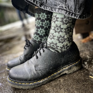 May include: Black leather lace-up shoes with a yellow stitch detail and a green and black patterned sock.