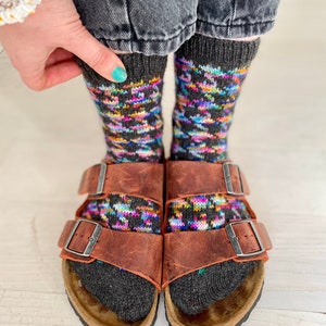 May include: A pair of brown leather sandals with two buckles on each strap. The sandals are worn with colourful patterned socks.