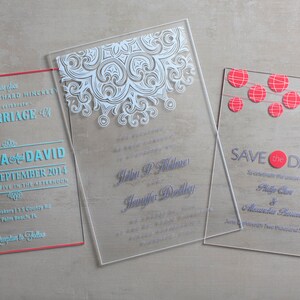 May include: Three clear acrylic wedding invitations with different designs. The first invitation has a white lace design and the text "The Marriage of Angela and David". The second invitation has the text "Helen P. Fisher and Jennifer Dollley". The third invitation has a red and white string of paper lanterns design and the text "Save the Date".