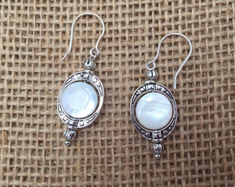 Earrings with glossy mother of pearl coin beads in oval pewter rings with little matching spacer beads on silver-filled ear wires.