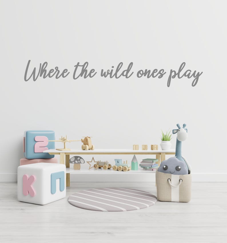 May include: A white shelf with wooden toys, books, and a stuffed giraffe. The shelf is in a room with a white wall that says "Where the wild ones play".