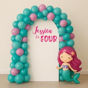 Może przedstawiać: Dekoracja na przyjęcie o tematyce syrenki z białym łukiem ozdobionym turkusowymi i różowymi balonami. Łuk ma różowy napis "Jessica is Four". Figurka syrenki z fioletowym ogonem i włosami znajduje się po prawej stronie.