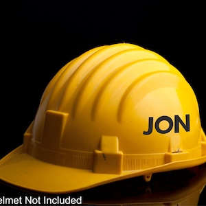 May include: A yellow hard hat with the name "JON" printed in black letters on the side.
