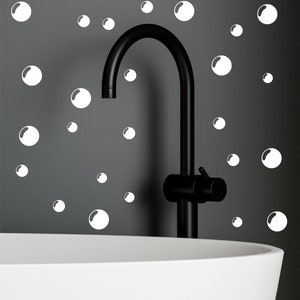 Może przedstawiać: Czarna bateria łazienkowa z białą wanną na pierwszym planie. Ściana za baterią jest ozdobiona białymi naklejkami w kształcie baniek.