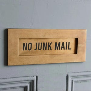 May include: A rectangular, brass-colored mailbox slot with the words "NO JUNK MAIL" in bold, black letters. The slot is mounted on a light blue door with paneling.