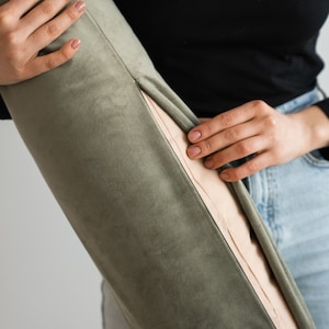 Könnte beinhalten: Olivgrünes Samt-Bolsterkissen mit hellbeigem Innenraum. Das zylindrische Kissen hat eine sichtbare Naht. Der Stoff wirkt weich und geschmeidig.