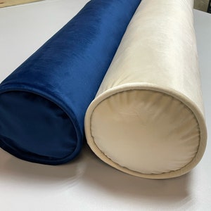 Könnte beinhalten: Zwei zylindrische Kissen, eines in Marineblau und eines in Creme, beide mit einem Bezug aus Samt.