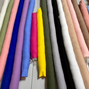 May include: A collection of 17 fabric swatches in various colors, including pink, blue, green, yellow, and white. The fabric swatches are arranged in a row on a white surface.