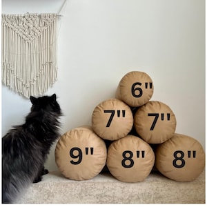 Könnte beinhalten: Ein Satz von sechs braunen zylindrischen Kissen in verschiedenen Größen. Die Kissen sind in Pyramidenform angeordnet, wobei das größte Kissen unten und das kleinste Kissen oben liegt. Die Kissen sind mit ihren Maßen in Zoll gekennzeichnet: 9", 8", 8", 7", 7" und 6".