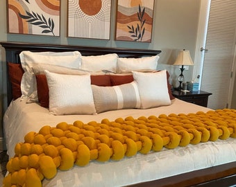 May include: A bed with a mustard yellow chunky knit blanket, white and rust-colored pillows, and three framed abstract art pieces. The bed has a dark wood headboard and is made up with white linens.