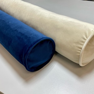 May include: Two cylindrical bolster pillows. One is a deep navy blue, the other is a soft cream color. Both are made of a plush, velvety fabric. The ends of the pillows are rounded and finished with a contrasting trim.