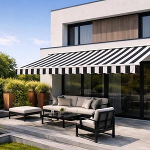 Puede incluir: Un toldo de terraza retr&aacute;ctil con rayas verticales negras y blancas, montado sobre una puerta corredera de cristal en un edificio blanco moderno. El toldo proporciona sombra sobre una zona de estar con sof&aacute;, sill&oacute;n y mesa de centro.
