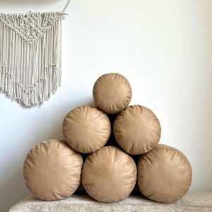 May include: A stack of six round brown throw pillows arranged in a pyramid shape. The pillows are made of a soft, plush fabric and are perfect for adding a touch of comfort and style to any room.