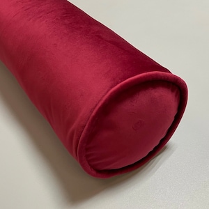 Könnte beinhalten: Ein langes, zylindrisches rotes Samtkissen mit abgerundetem Ende.