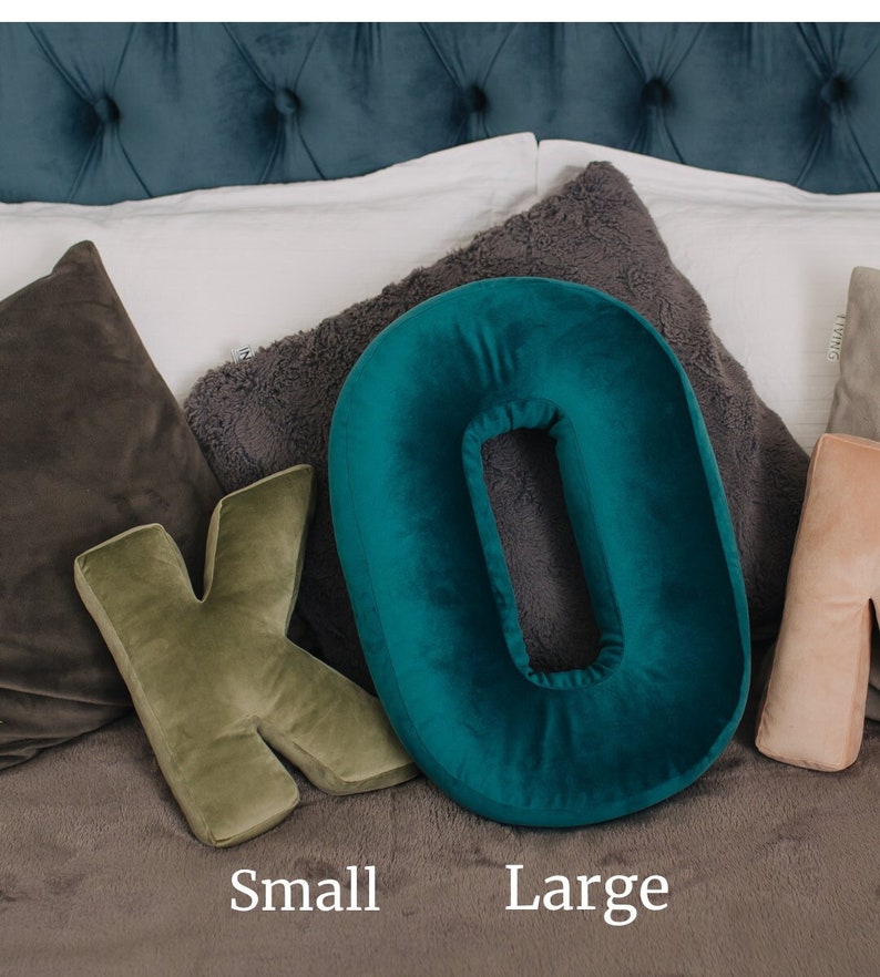 May include: A plush velvet throw pillow shaped like the letter K in olive green and a plush velvet throw pillow shaped like the letter O in teal. The text Small is positioned below the K pillow and the text Large is below the O pillow.