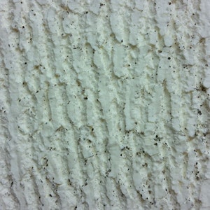 May include: White textured wall with a pattern of vertical lines and small black specks.