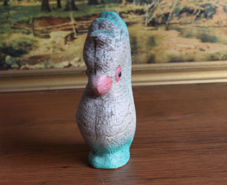 May include: A vintage bird figurine with a textured, speckled gray body, a pink beak, and a turquoise base and head crest. The bird has a single black eye. The figurine is likely made of ceramic or a similar material.