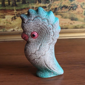 May include: A vintage ceramic parrot figurine with a textured surface. The bird has a light gray body with turquoise accents on the head and base. It features a red beak and eye, and is a decorative item.