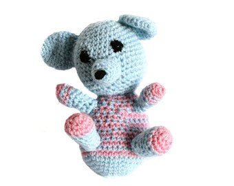May include: A handmade crochet bear in light blue and pink. The bear has a light blue head, ears, arms, and legs. The body is light blue with pink stripes. The bear has black eyes and a black nose. A cute, soft toy.