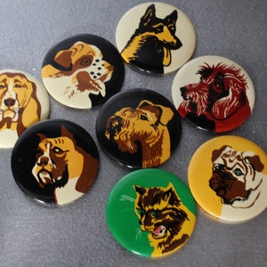 May include: A selection of eight circular pin badges showcasing illustrations of different dog breeds and a cat. The badges have a glossy finish and are set against a neutral backdrop. The dog breeds include a German Shepherd, a pug, and a terrier.