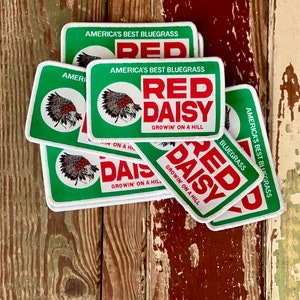 May include: A collection of rectangular patches with a green border and white background. The patches feature the text "AMERICA'S BEST BLUEGRASS" and "RED DAISY GROWIN' ON A HILL" in red. A circular graphic of a Native American headdress is also present.