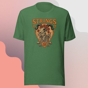 May include: Green t-shirt with a graphic design featuring the word "STRINGS" in orange, a skull with horns and flowers, and the number "33". The design is in a triangle shape with mushrooms at the bottom.