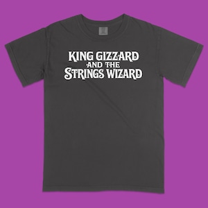 May include: A charcoal gray short-sleeve t-shirt featuring the white text "KING GIZZARD AND THE STRINGS WIZARD" printed across the chest. The garment has a crew neckline and a standard fit, showcasing a clean design with bold, stylized lettering.