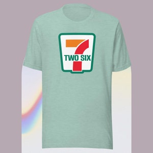 Puede incluir: Una camiseta azul claro con un logotipo verde y rojo que presenta el número 7 y el texto "TWO SIX".
