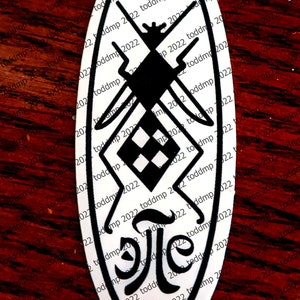 May include: A white oval sticker with a black and white design. The design features a stylized insect with a checkered pattern on its body and an arrow pointing upwards. The sticker is on a red wooden surface.