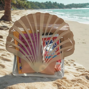 May include: A clear, seashell-shaped pouch filled with various items, including a pink pouch, a packet of wet wipes, and a small book with the text "Butts deserve better". The pouch is on a sandy beach with the ocean in the background.