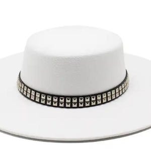 Pode incluir: Um chapéu fedora branco com uma faixa preta adornada com tachas piramidais prateadas.