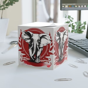 May include: A white notepad with a red, white, and black illustration of an elephant. The elephant is walking forward with its trunk raised. The illustration is surrounded by a wreath of leaves and a red circle.