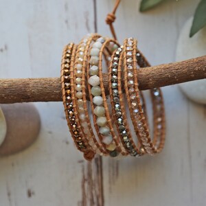 May include: A multi-strand leather wrap bracelet with brown leather cord and various beads, including light green, brown, and clear glass beads. The bracelet is wrapped around a branch.