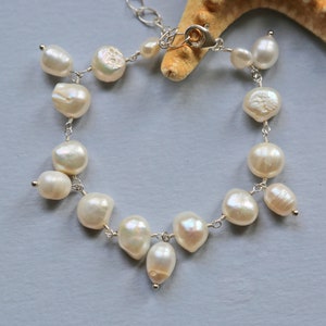 May include: A delicate pearl bracelet with a silver clasp. The bracelet features a cluster of white pearls in a cascading design.